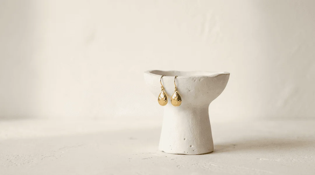 Gold drop earrings styled elegantly on a white plaster display pedestal