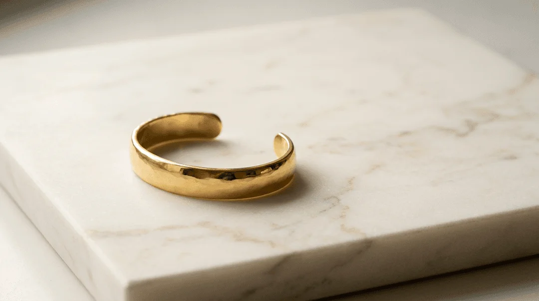 Elegant gold cuff bangle bracelet on a smooth cream marble slab