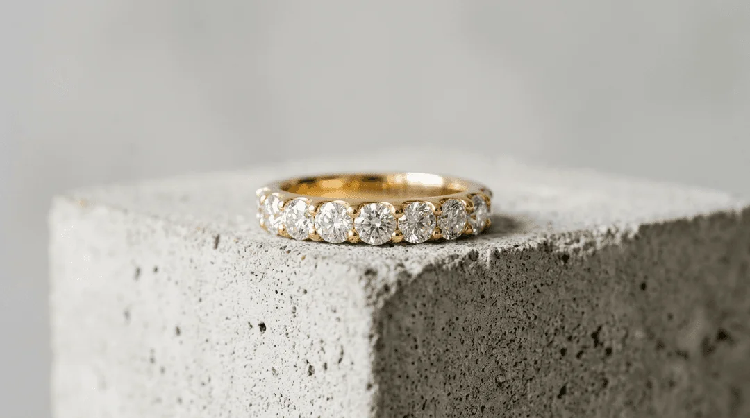 Gold diamond wedding band ring on a structured concrete block showing soft ambient reflections