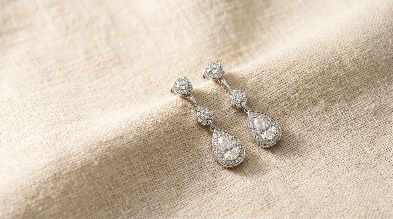 Studio flat lay of elegant diamond drop earrings on warm natural linen backdrop