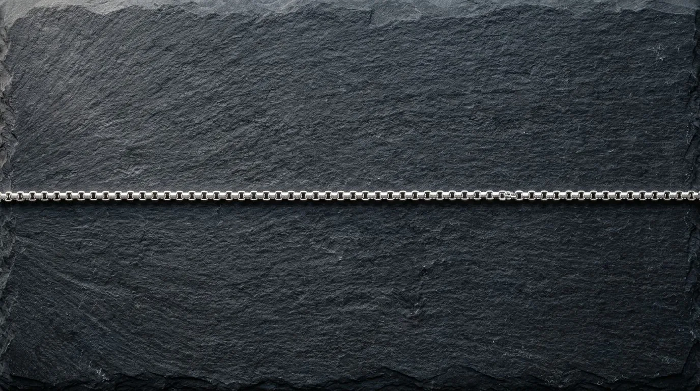 Silver chain necklace laid in a straight line on dark slate to showcase fine links and textures