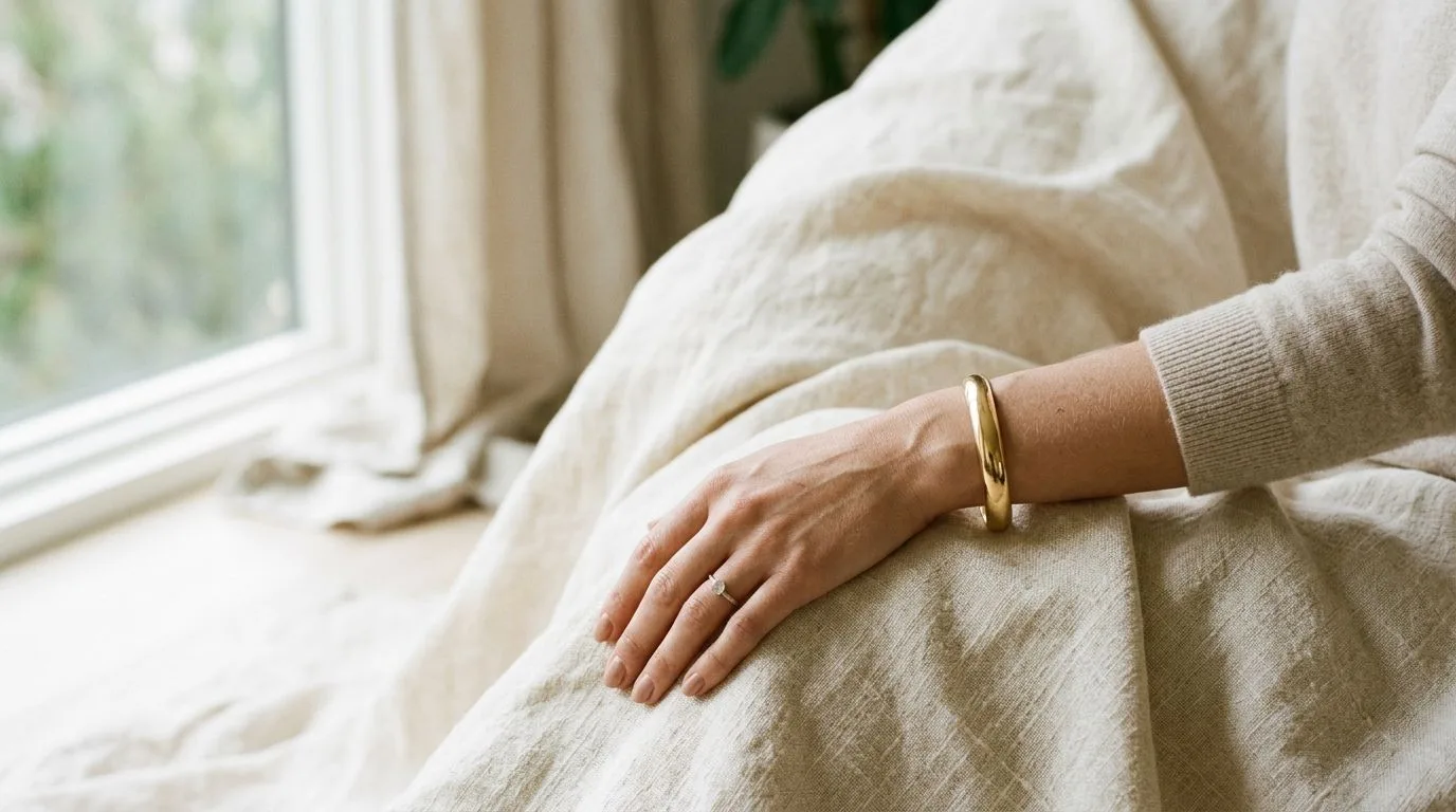 On-model gold cuff bangle bracelet resting against natural cream linen in soft window light